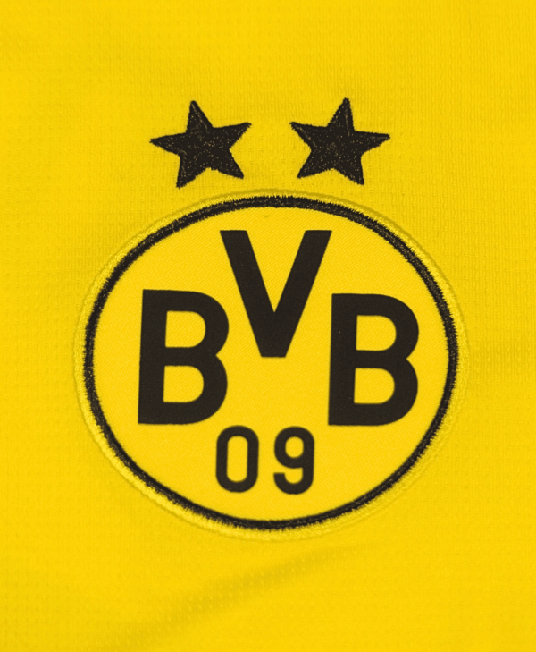 Imagen de un zoom del detalle del escudo del Borussia Dortmund, de la camiseta local del club para la temporada 2023-2024.