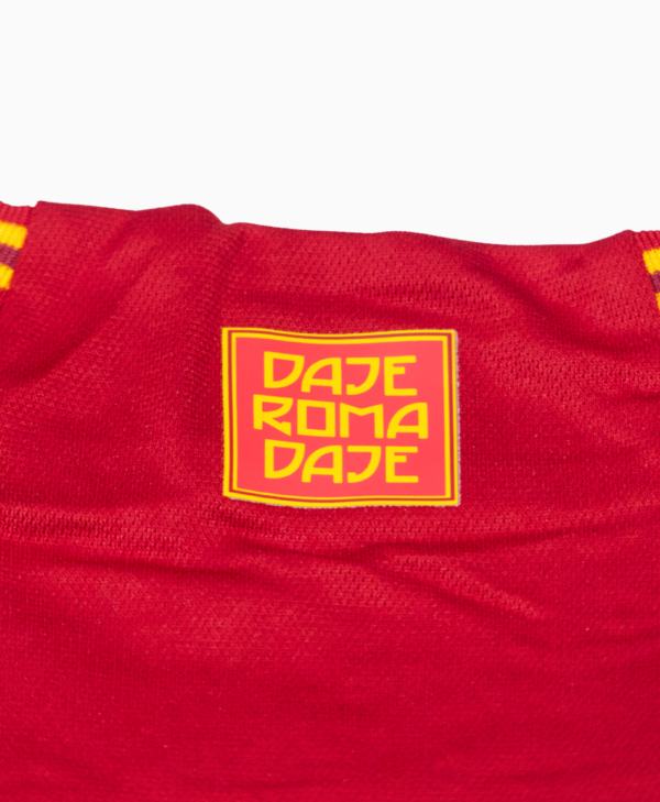 Imagen de un zoom en el detalle del cuello que dice "Daje Roma Daje" en la camiseta local de la Roma para la temporada 2023-2024.