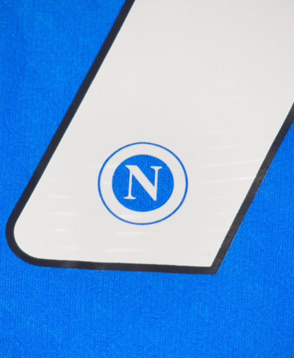 Imagen de un zoom al detalle del escudo del Napoli en la camiseta local para la temporada 2023-2024.